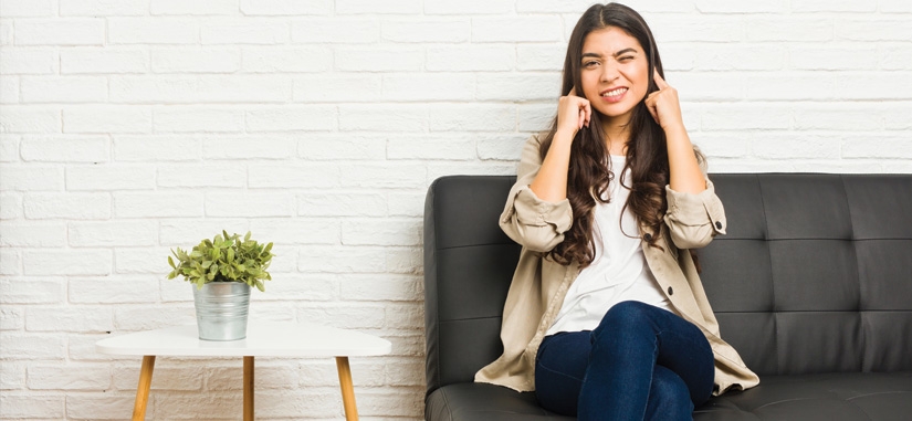 Femme sur son canapé qui se bouche les oreilles