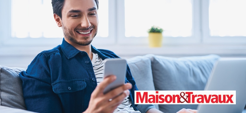 homme assis sur son canapé qui regarde son téléphone en souriant