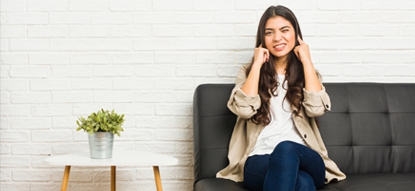 Femme sur son canapé qui se bouche les oreilles