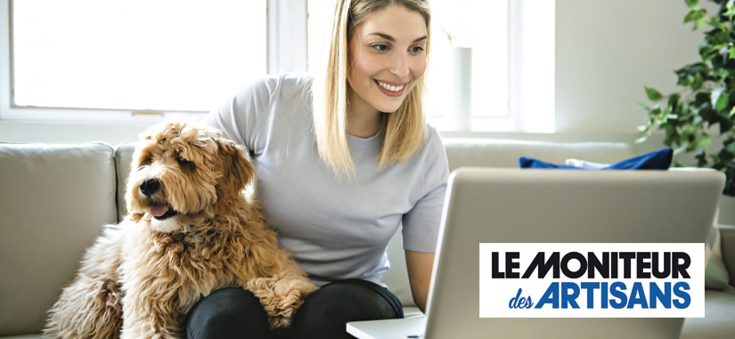 jeune femme assise sur son canapé qui regarde son ordinateur avec son chien à coté